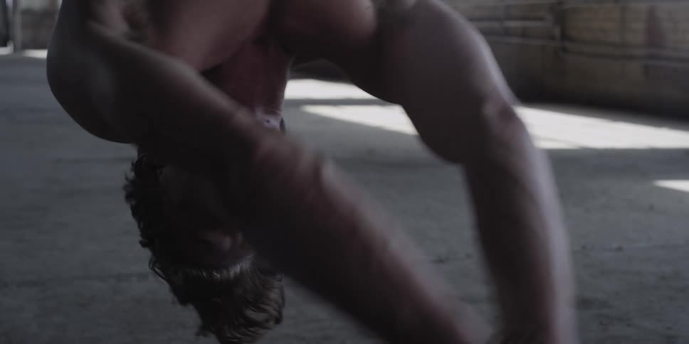Scared shirtless nervous tied up man hanging upside down inside a warehouse