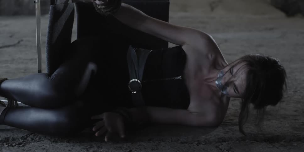 A woman bound to a fallen chair with masking tape over her mouth cries and struggles to get free while looking into the camera