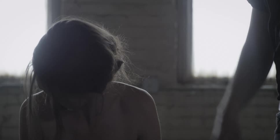 A man in a room grabbing a womans hair with her mouth duct taped with a wall and window in the background