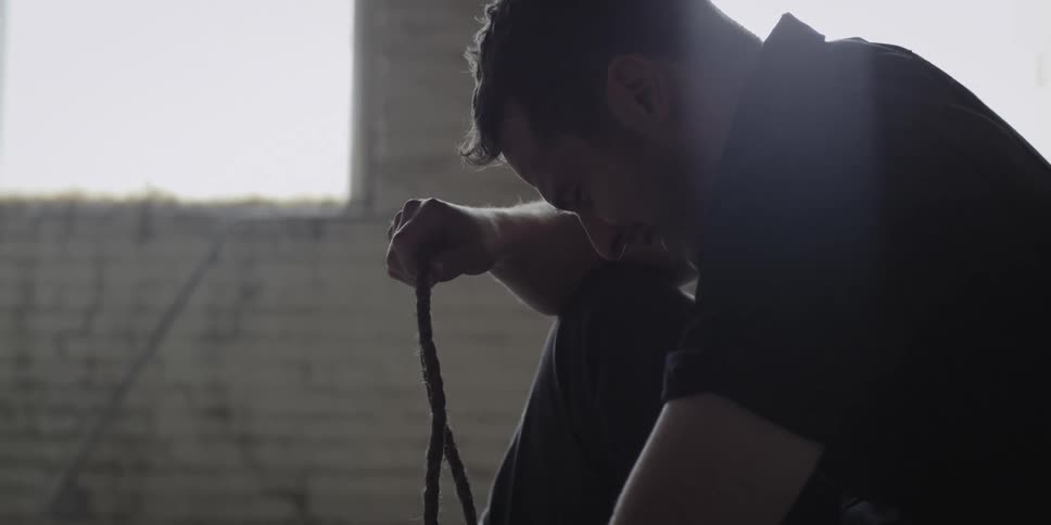 A man leans forward in pain holding a rope
