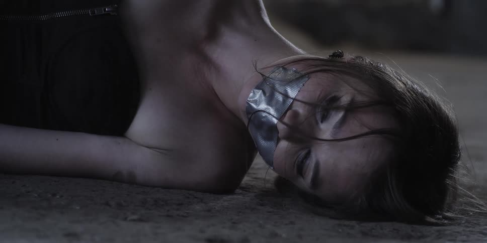 A female with her mouth taped shut is laying on the ground