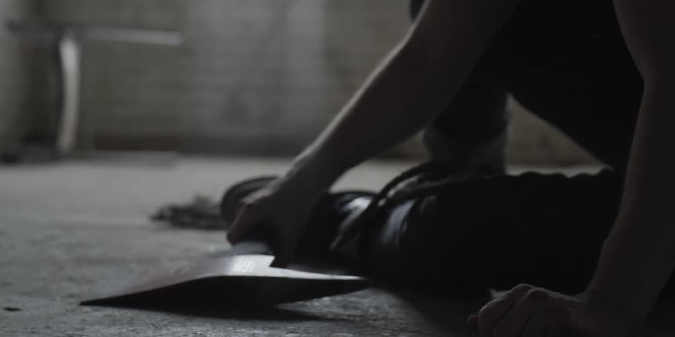 A man is sitting on a floor and he reaches to pick up an axe that is resting on his foot
