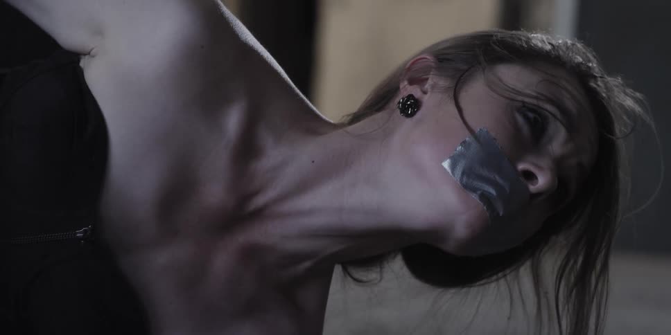 A woman with duct tape over her mouth struggles against her constraints