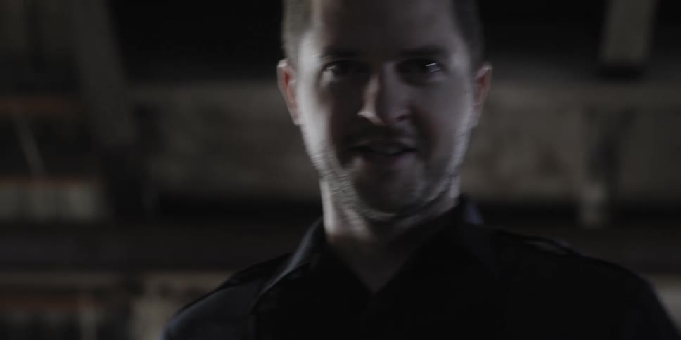 Man walks inside a warehouse looking menacingly at the camera
