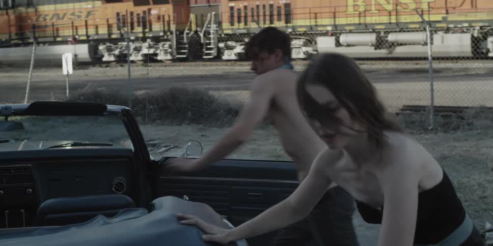 A woman helps a man get to a car near a train