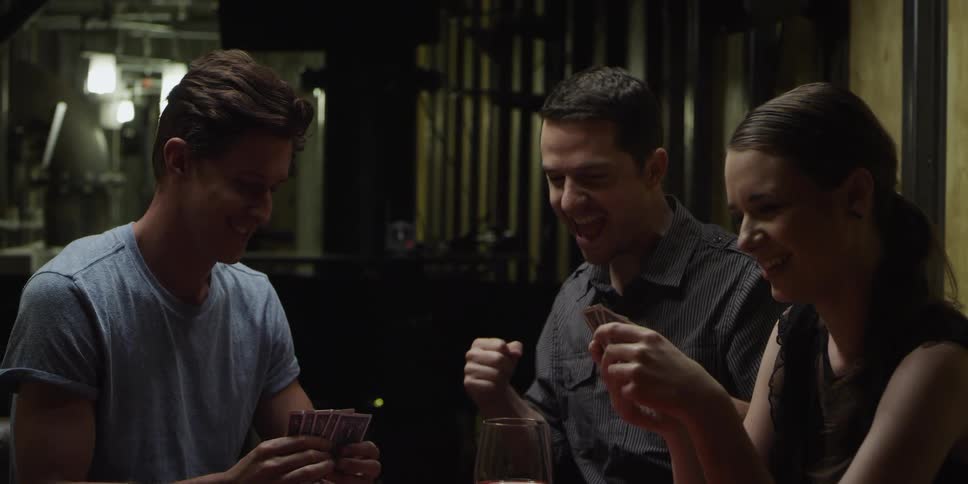 Friends sit around table with drinks playing card game