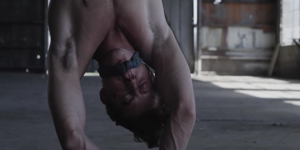 A man wiggles his arms and tried to remove a gag from his mouth as he hangs upside down and tied up