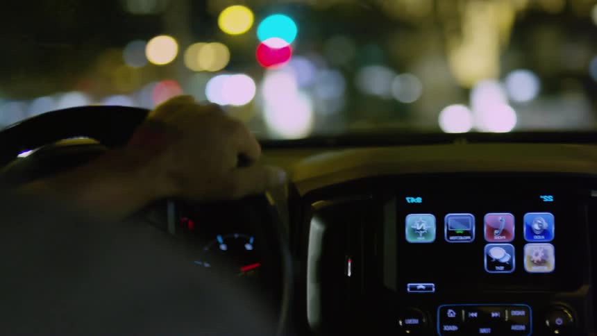 Person holds the steering wheel to control the vehicle and touches the screen at night