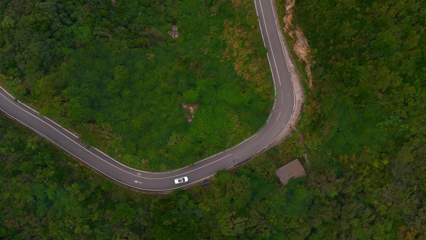 A vehicle is driving on a winding road through a heavily forested area