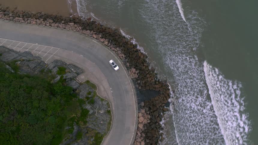 Aerial view of a white car driving on a coastal road