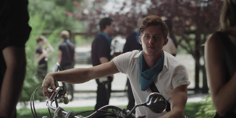 Young man sitting on a motorcylce stands up and walks towards the camera