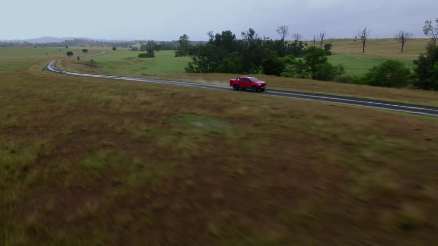 A red truck is traveling on a wet country road with trees along the roadside