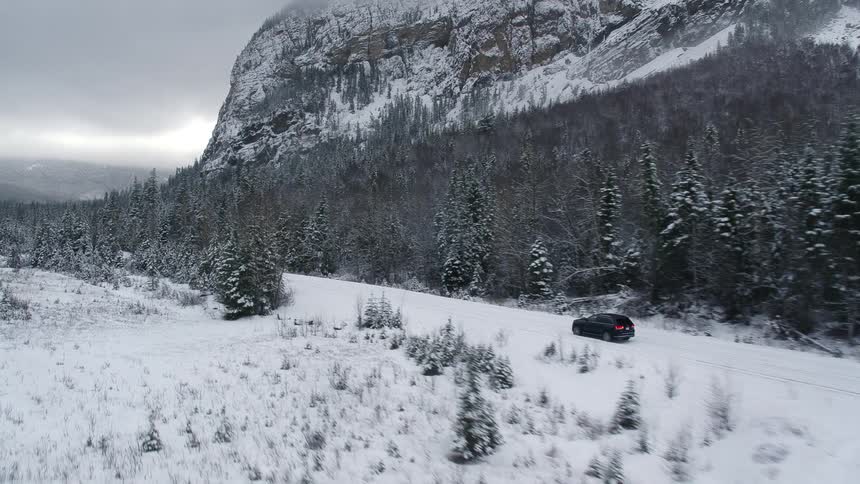 Black car driving on a road through the pine forest at winter near the mountain