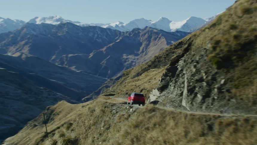 Aerial view of a red vehicle driving on a road on the mountains