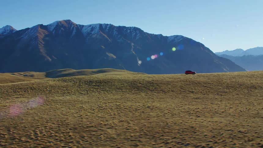 An suv travels on an empty road with mountain behind and sunshine glaring