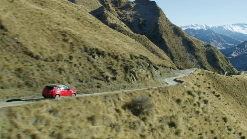 A red van travels on a mountain road with a mountain range in the distance