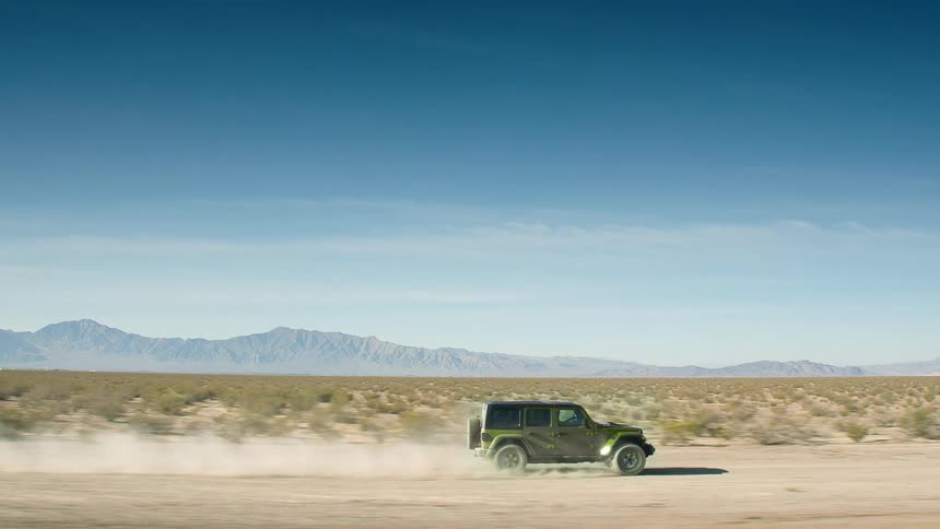 Green all terrain vehicle driving on a dirt road through the desert