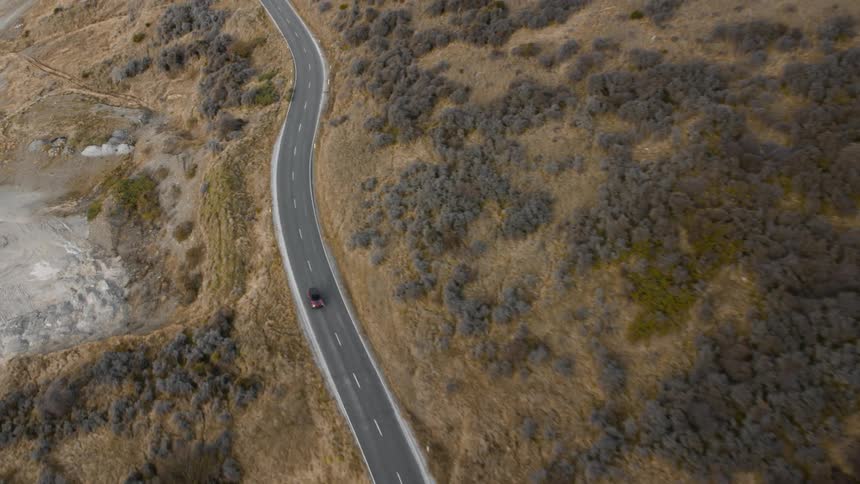 An aerial view of a car driving on a road next to a wide open field