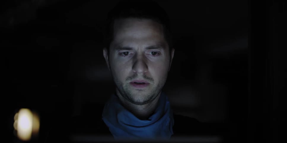 A light shines on a mans face as he sits in a dark room