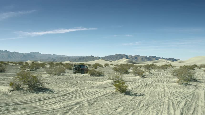 A vehicle driving in a desert with a mountain range the sky and clouds in the background