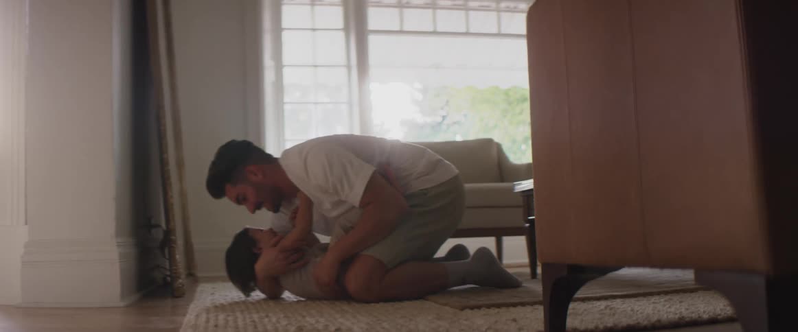 A child in a room running up to a man and hugging in with a wall a door and a window in the background