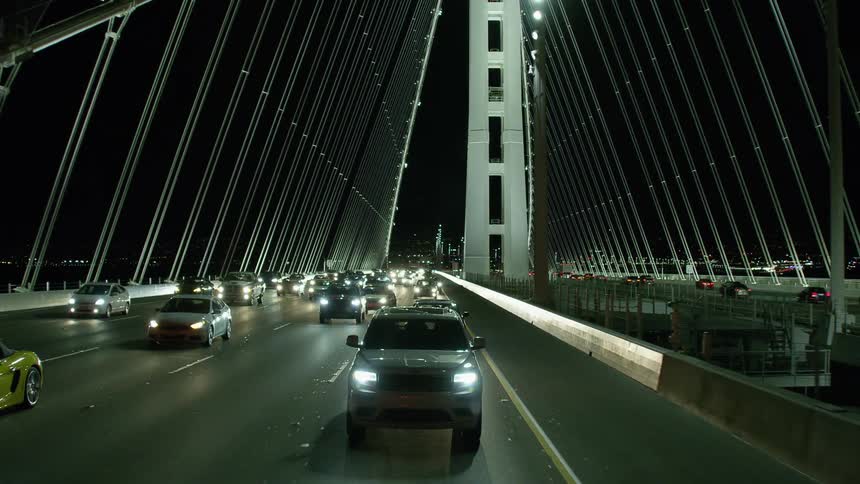 Vehicles driving on a bridge with the sky and buildings in the background