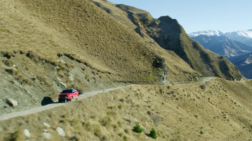 A red van travels on a mountain road with a mountain range in the distance