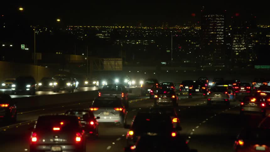 A highway with vehicles signs and streetlights with buildings in the background