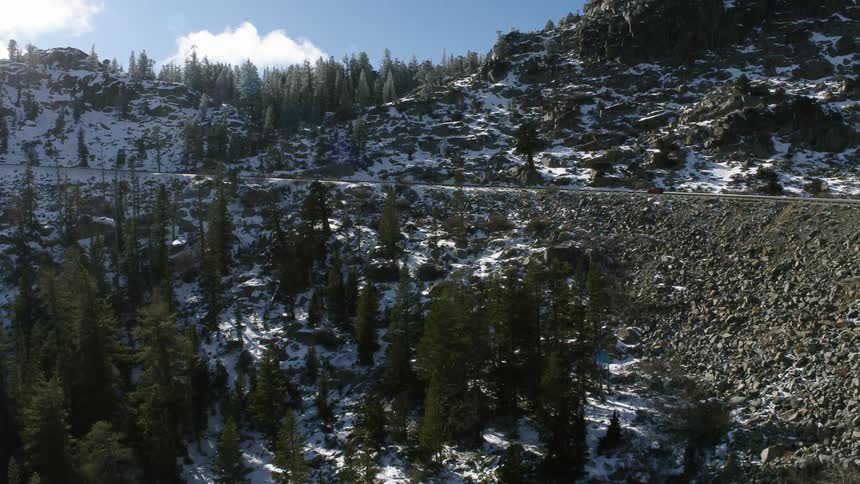 A red automobile travels on a mountain road surrounded by trees on a winter day