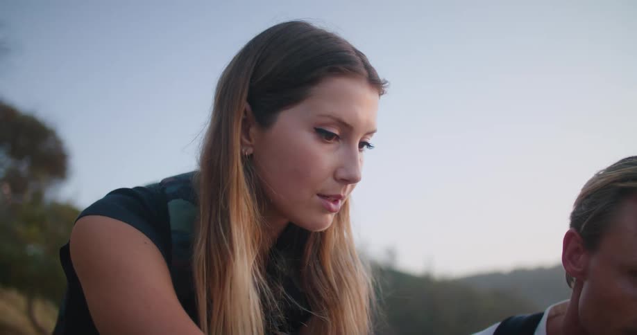 Couple sitting on the rocks close to a beach checking a tablet at sunset