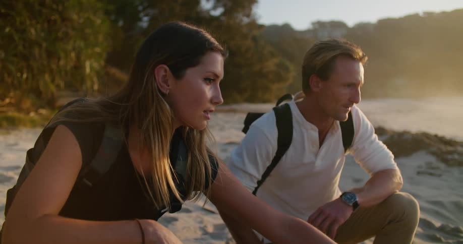 Man and woman crouch on beach discussing water line