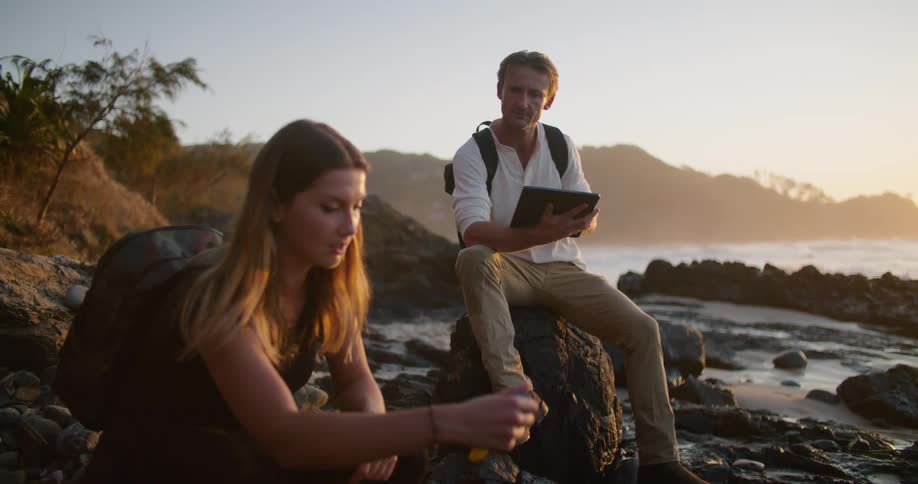 A man and woman test the water in the rocks coming in from the ocean