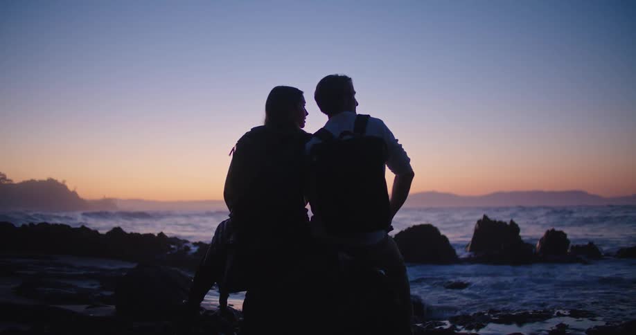 A couple sit on the rocks by the shore