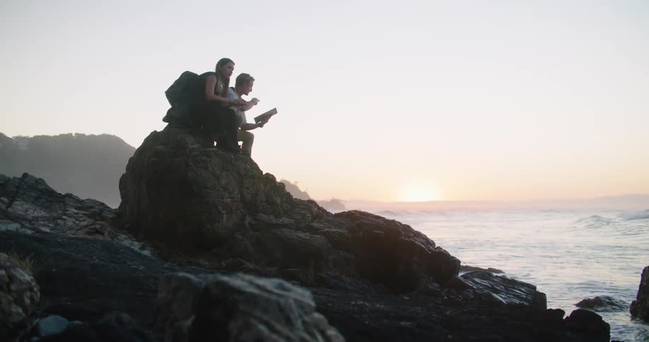 Young couple sitting over a rock near the beach in front of the ocean at sunset