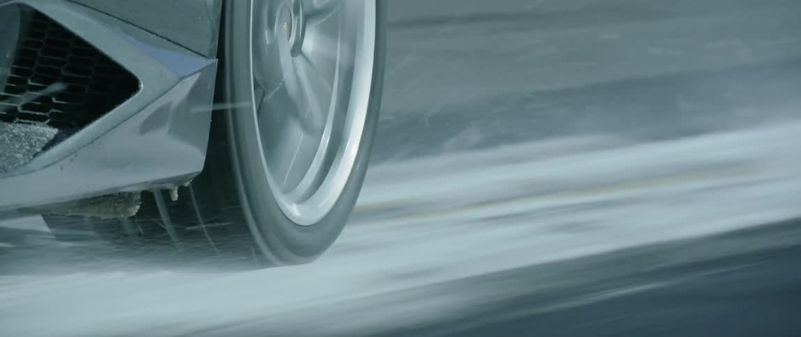 The tire of a black car speeding down a road