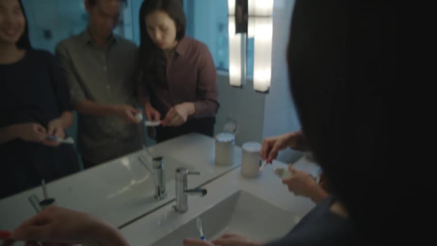 A man a woman and two girls in a bathroom with toothbrushes and toothpaste in front of a sink and mirror