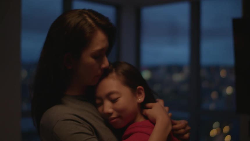 A daughter walks into her mothers arms for a hug in front of large windows showcasing downtown