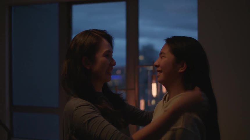 A woman in a girl hugging in a room with a wall and window in the background