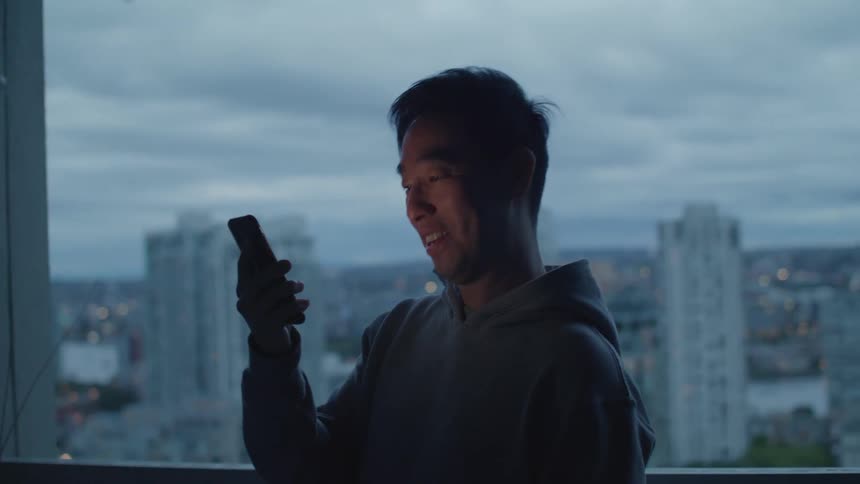 A man laughs and nods as he talks on his cell phone in front of a large window overlooking a city