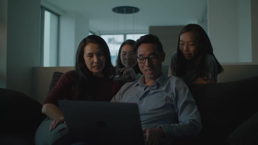 Afamily is sitting on a couch looking at a computer and smiling and waving