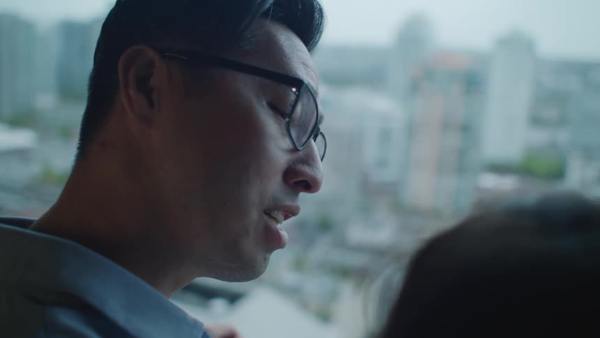 A man and a girl on a balcony with buildings the sky and clouds in the background