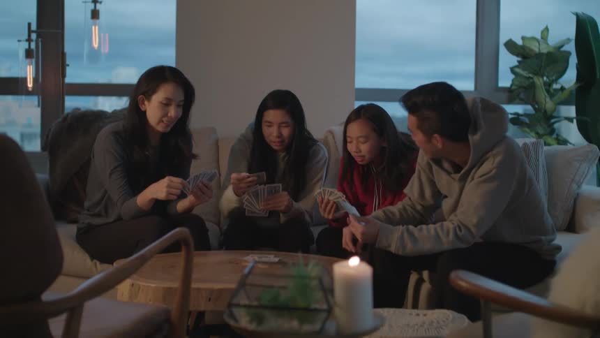 A family of four sits on a sofa laughing and playing a card game
