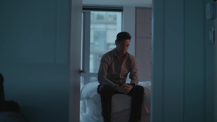 A man is sitting on a bed with his head in his hands then he stretches