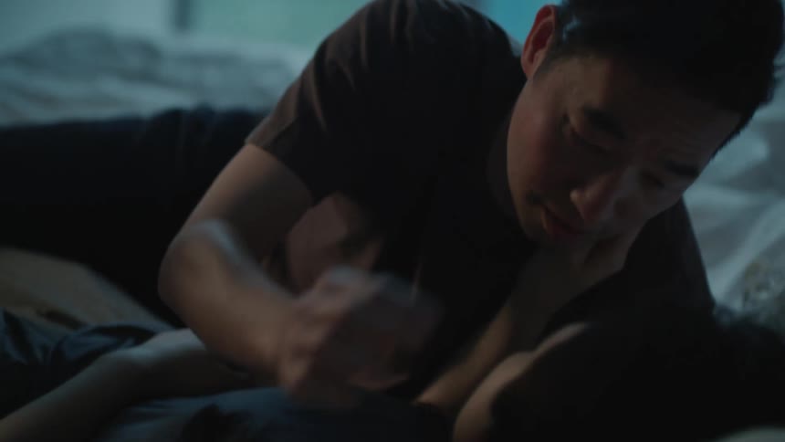 A man leans over to kiss a woman as they lay in a bed
