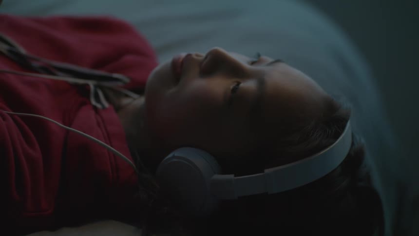 A girl in a room listening to headphones and laying in bed
