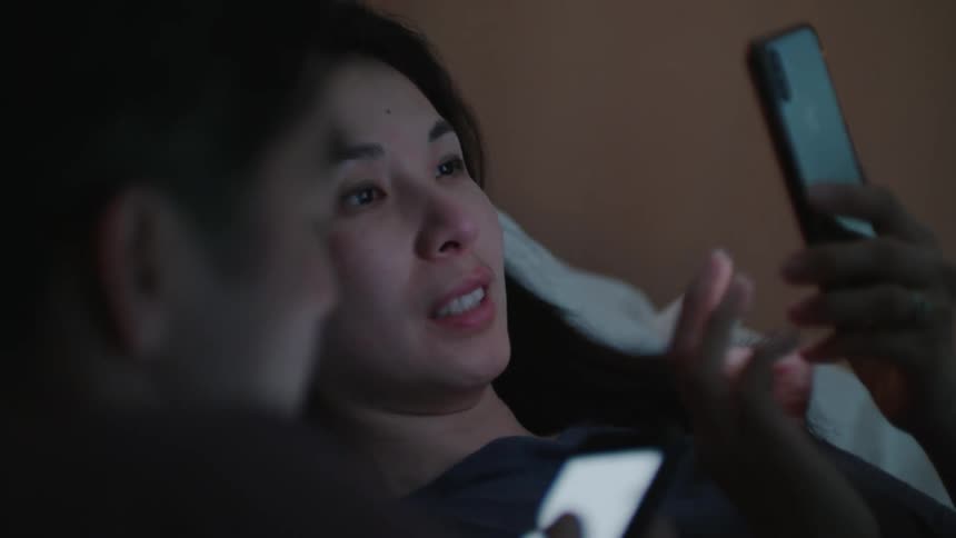 A woman and a man are lying on a bed using cell phones