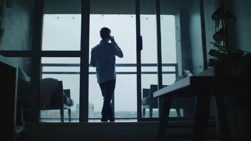 A man talks on the phone while standing on his balcony downtown