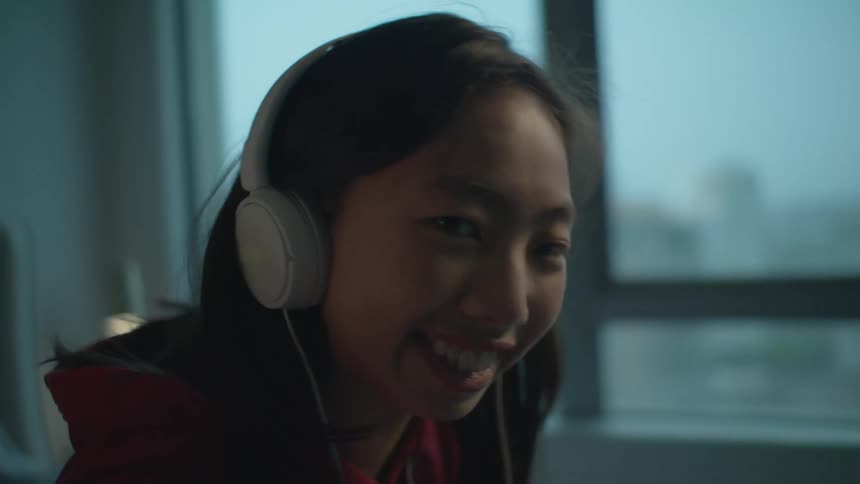 Teenage girl with red zip up and headphones smiles at the camera