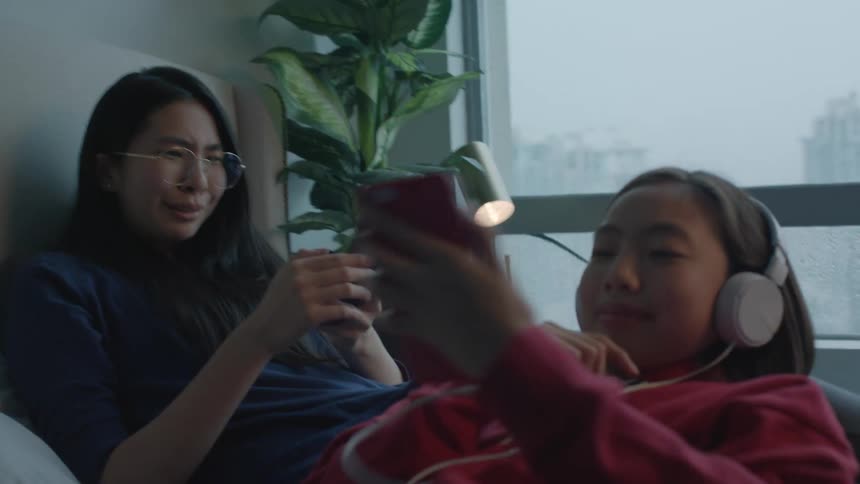 Teenage girls with red zip up blue sweater and glasses use smartphones with headphones