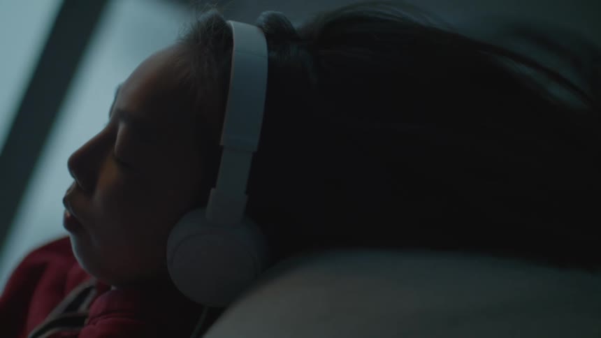 Woman lies on back listening to headphones near window